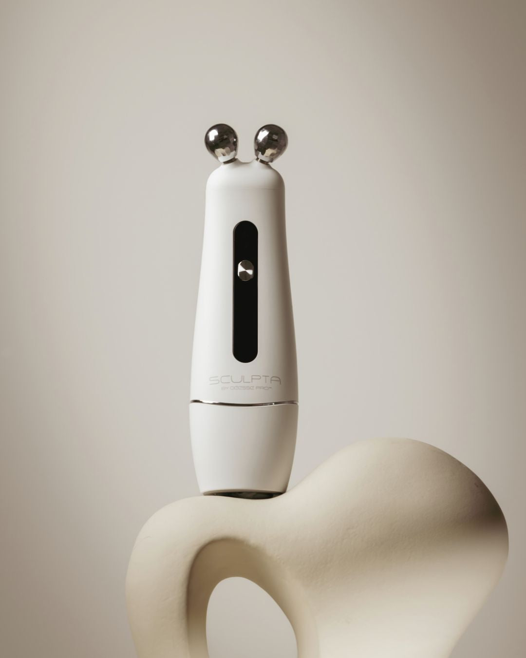 Déesse PRO Sculpta handheld device with two metallic spherical probes on abstract beige sculpture